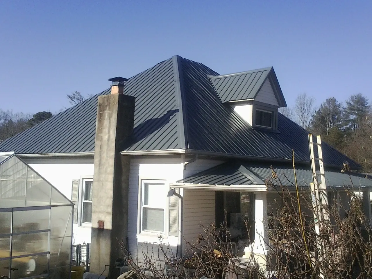 Dark blue standing seam metal roof on a white farmhouse with dormer — Slate & Tile Roof Repair by Roofing Brothers in Burleson
