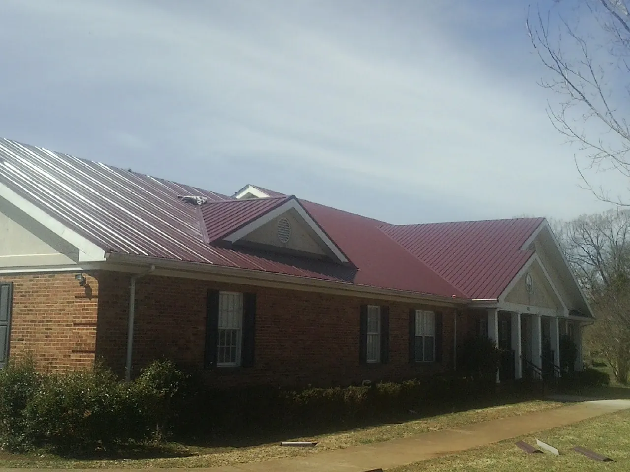 Red metal roof with gabled entries on a long brick building, from a Hail Damage Roof Repair job in Burleson