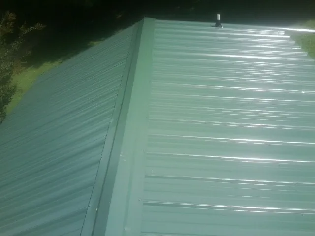 New green metal panels meeting at the ridge of a roof — Flat Roof Repair work by our crew in Burleson