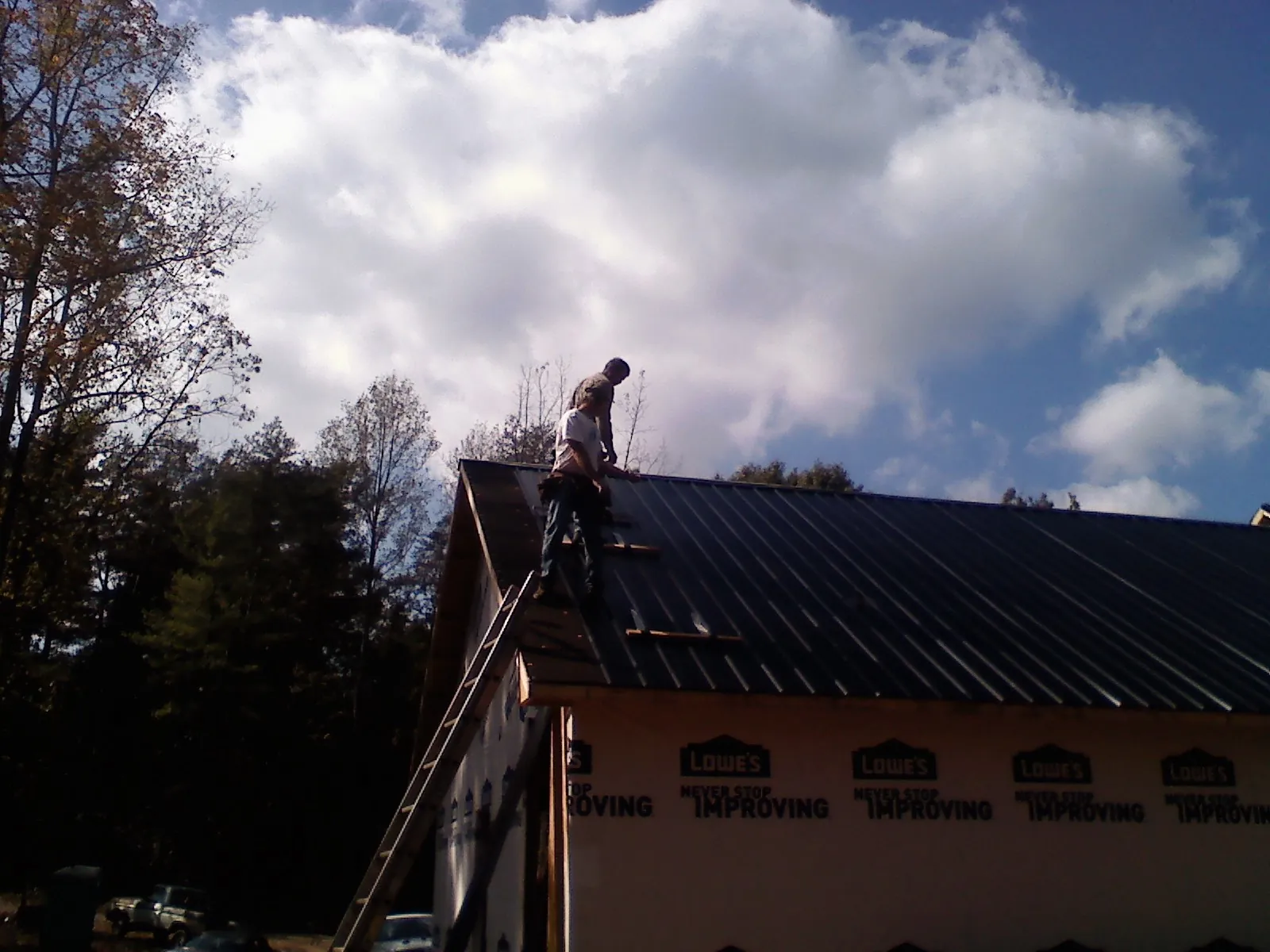 Roofer fastening dark metal panels high against a cloudy sky, from a Roof Inspection job in Burleson
