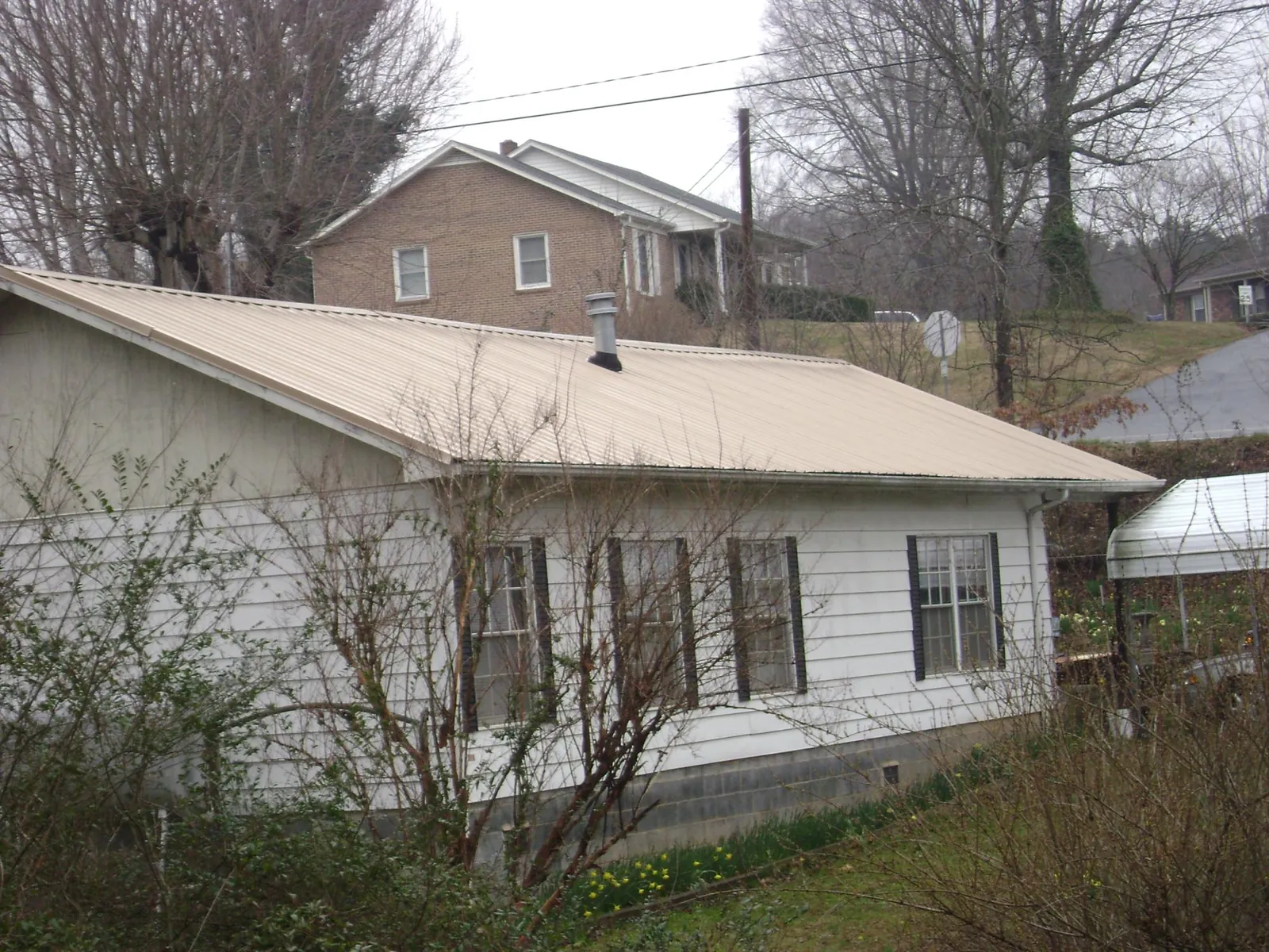 Tan metal roof on a white sided house set into a hillside — Commercial Roofing by Roofing Brothers in Burleson